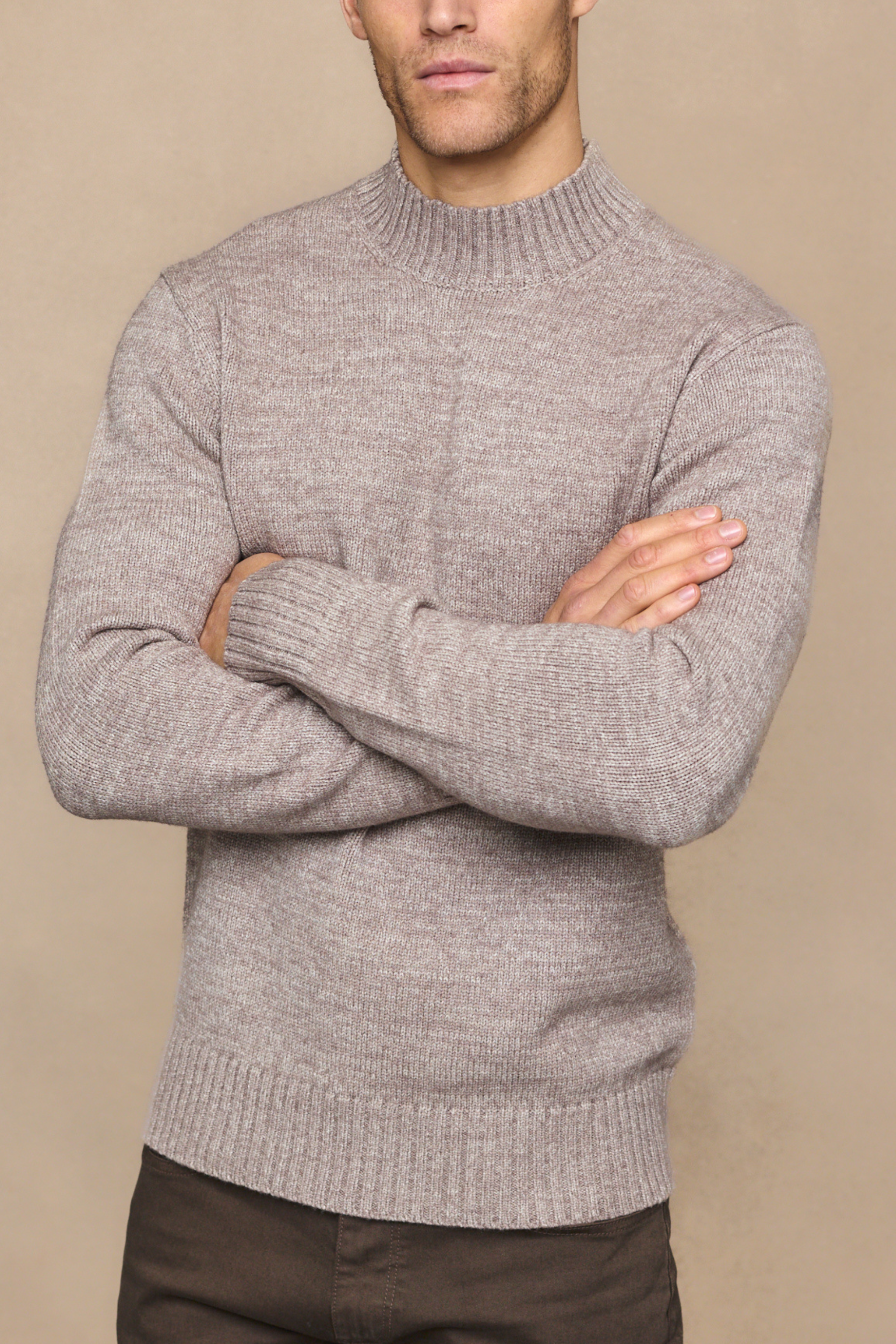 Man wearing a gray sweater with arms crossed against a beige background